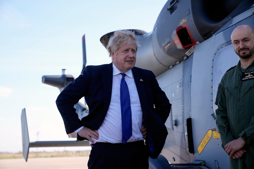 British Prime Minister Boris Johnson stands in front of a helicopter