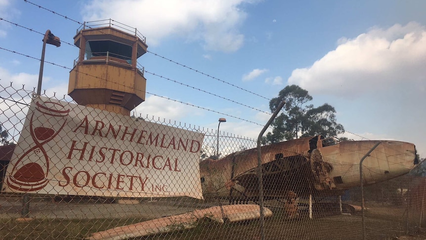A photo of the Arnhem Land Historical Society sign with the tower and an old plane behind a fence.