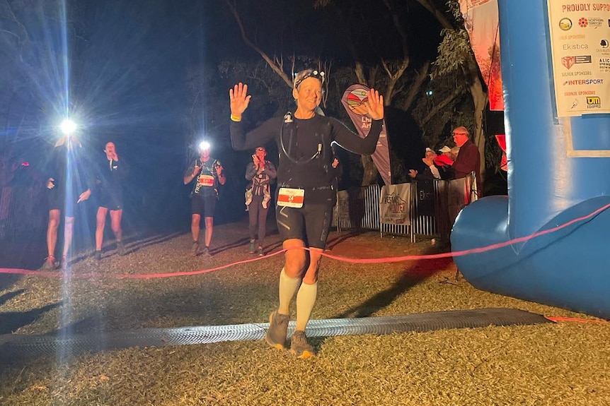 A woman walks through a red ribbon with her hands up, after crossing the finish line first.