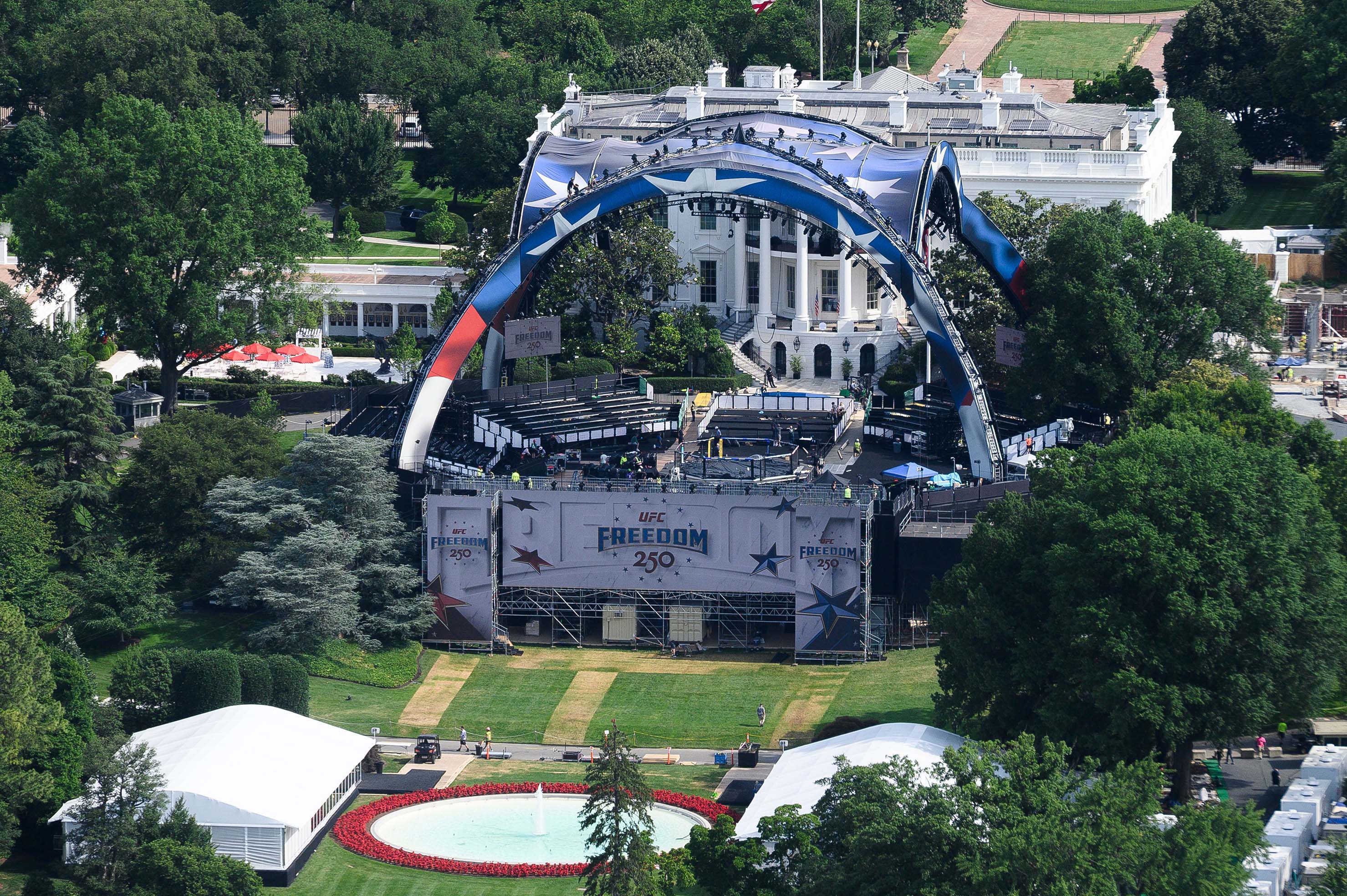 A metal structure and fighting ring are surrounded by seating on the lawn in front of the white house