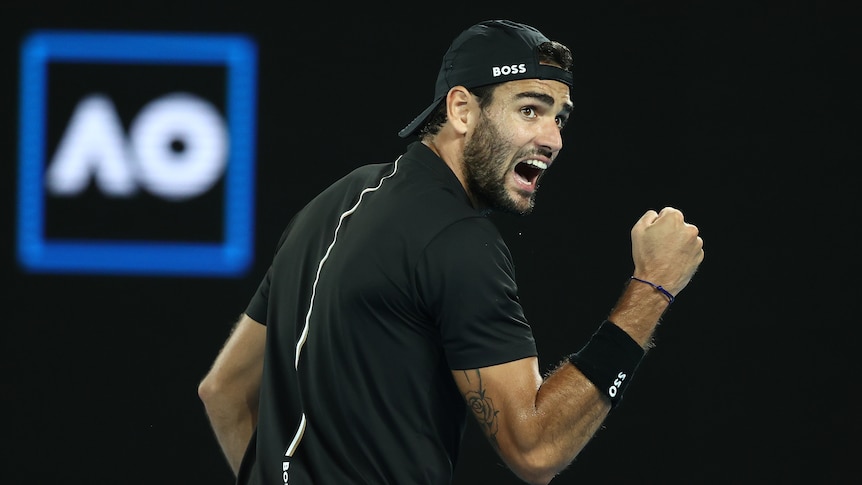 An Italian male tennis player pumps his right fist as he celebrates winning a point.