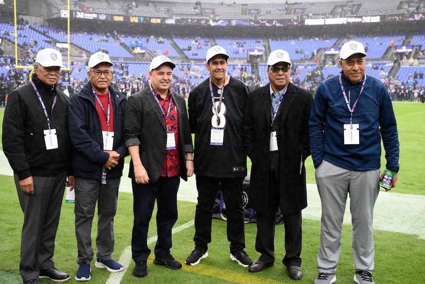 A group of Pacific Islands leaders pose for a photo at an American football game. 