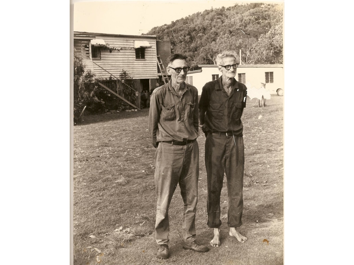 Dois homens mais velhos em uma foto em preto e branco, um deles sem sapatos.