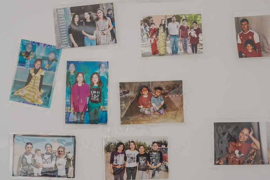 Photos of friends and family members are stuck to a white bedroom wall.