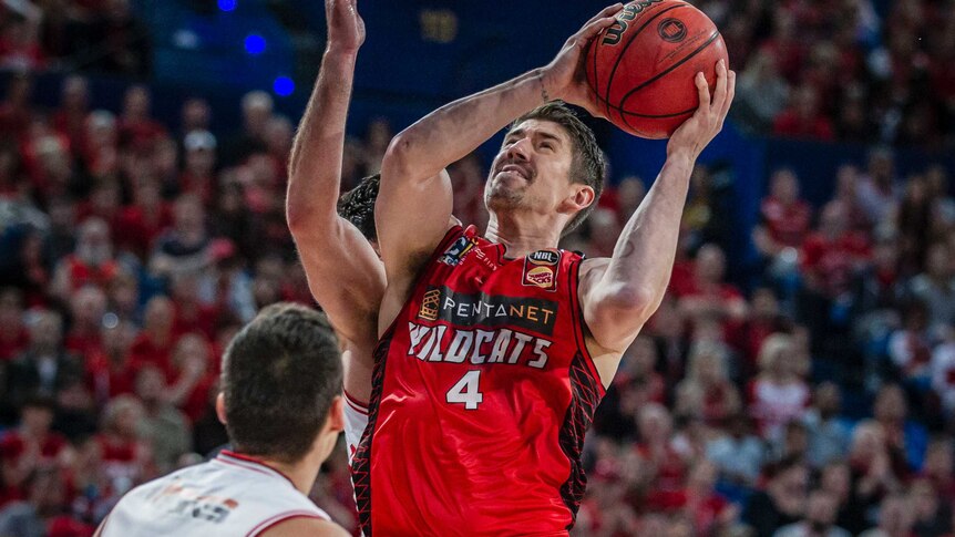 Perth Wildcats forward Greg Hire jumps towards the basket between two Illawarra Hawks players with the ball in his hands.