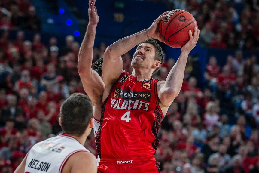 Perth Wildcats forward Greg Hire jumps towards the basket between two Illawarra Hawks players with the ball in his hands.