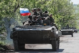 Pro-Russian soldiers sit atop a tank with Russian flag flying.