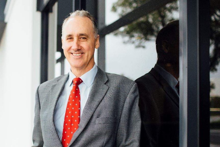 David Honey in a grey suit with a red tie outside the front of a building.