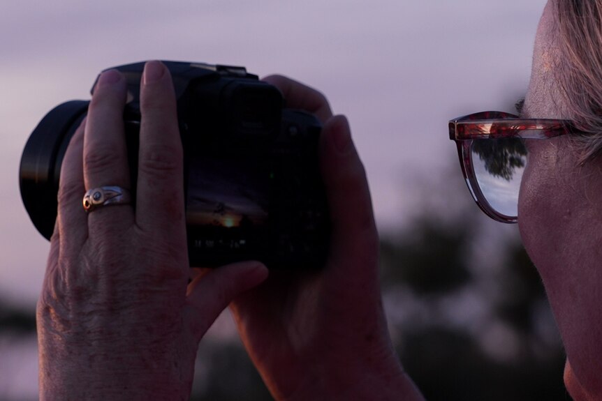 a woman wearing glasses takes photos with a digital camera