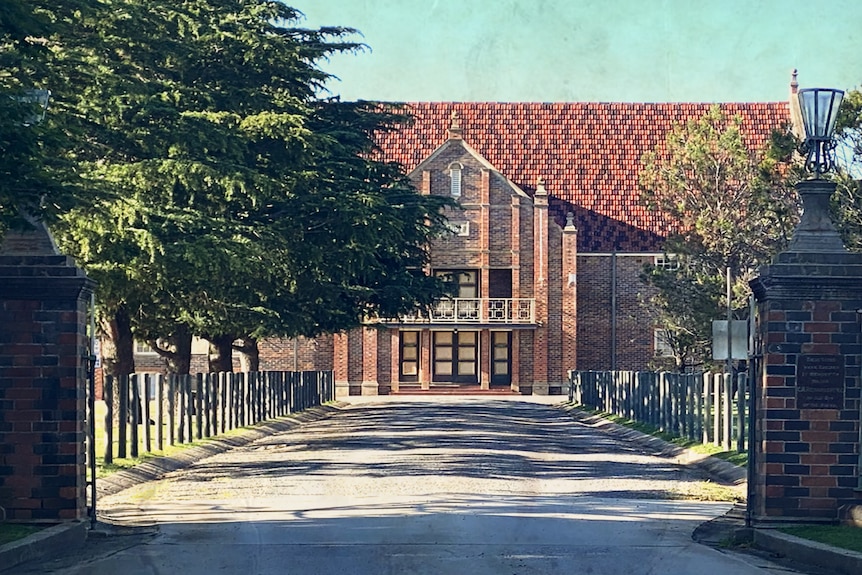 A large, multi-storey brick building at the end of a long driveway lined by trees.