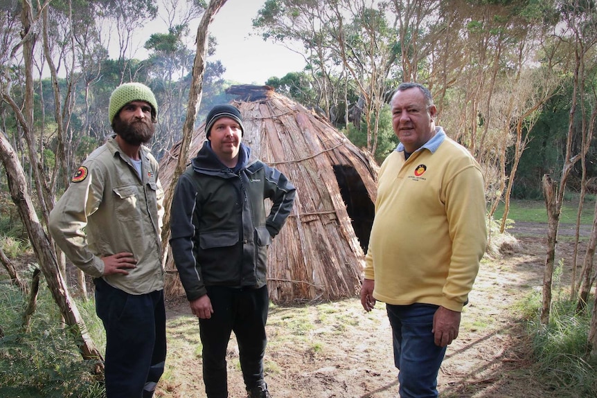 Brenton Brown, Tim Lowery and Graeme Gardner stand in front of an Aboriginal hut.