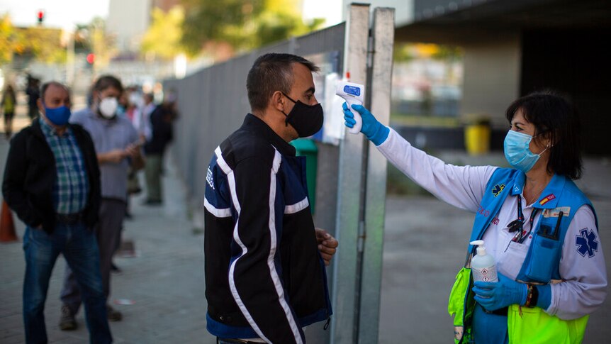 health worker checks the temperature of a man prior to a rapid antigen test for COVID-19 in Madrid.