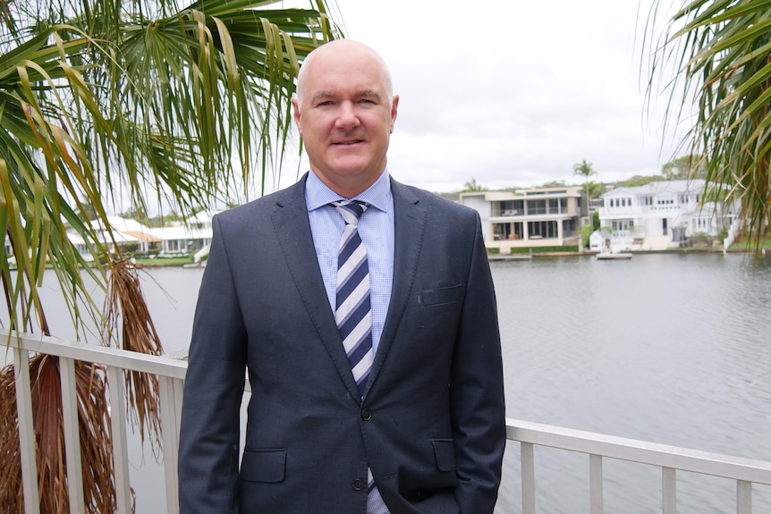 CoreLogic's Tim Lawless in a blue suit stands on a bridge with expensive homes in background.