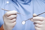 Close up of dentist's hook and mirror being held in gloved hands