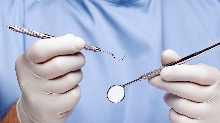 Close up of dentist's hook and mirror being held in gloved hands
