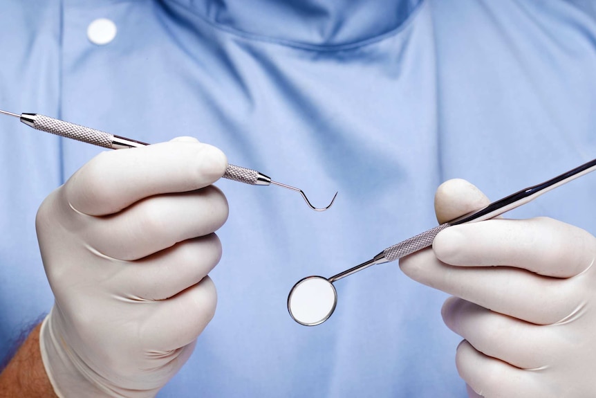 Close up of dentist's hook and mirror being held in gloved hands