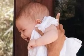 Meghan holds a giggling Lilibet in the air as Harry holds Archie on his knee