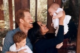 Meghan holds a giggling Lilibet in the air as Harry holds Archie on his knee