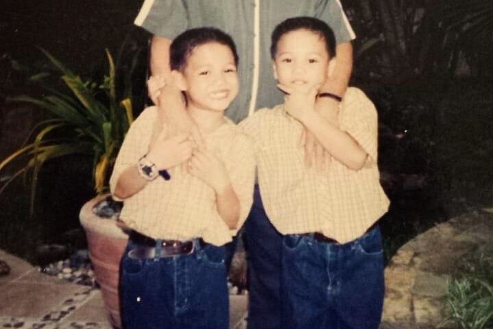 Anton poses for a photo with his twin brother in matching jeans and shirts as kids.