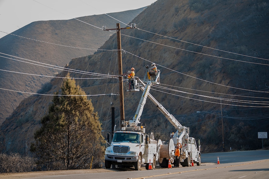 Technicians repairs a power line in a fire-charred landscape