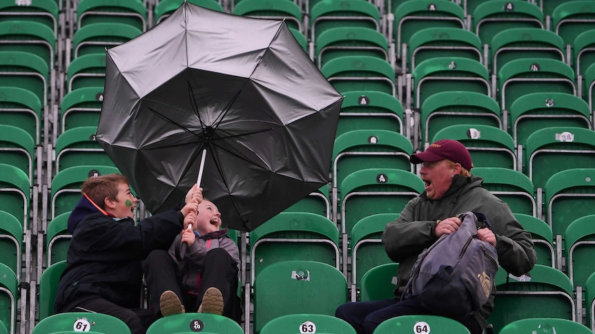 Two boys laugh as their umbrella flips with a shocked man looking on.