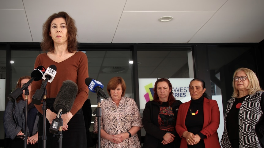 Alison Evans wears a brown top and a solemn expression, with women behind her.