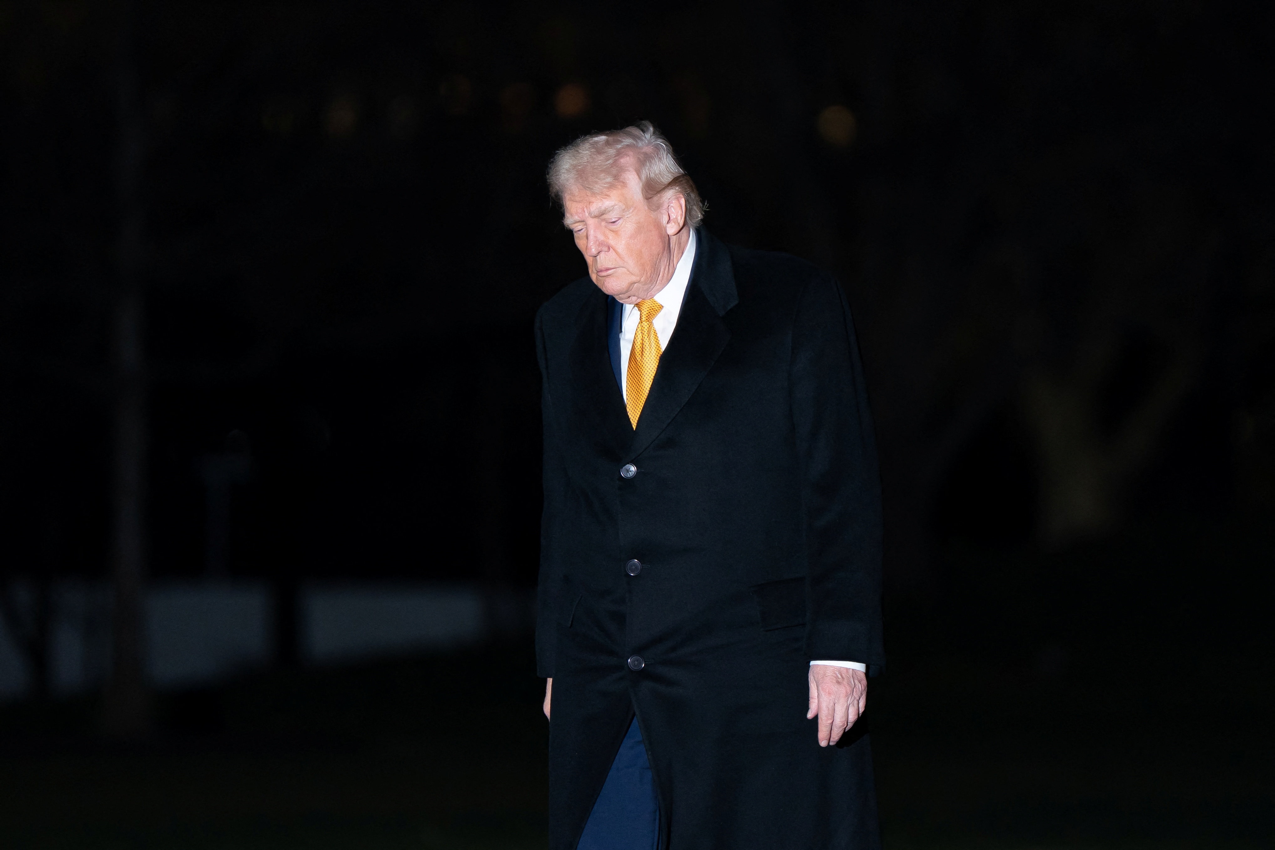 Trump caminha com os olhos baixos, vestido com um sobretudo de lã.