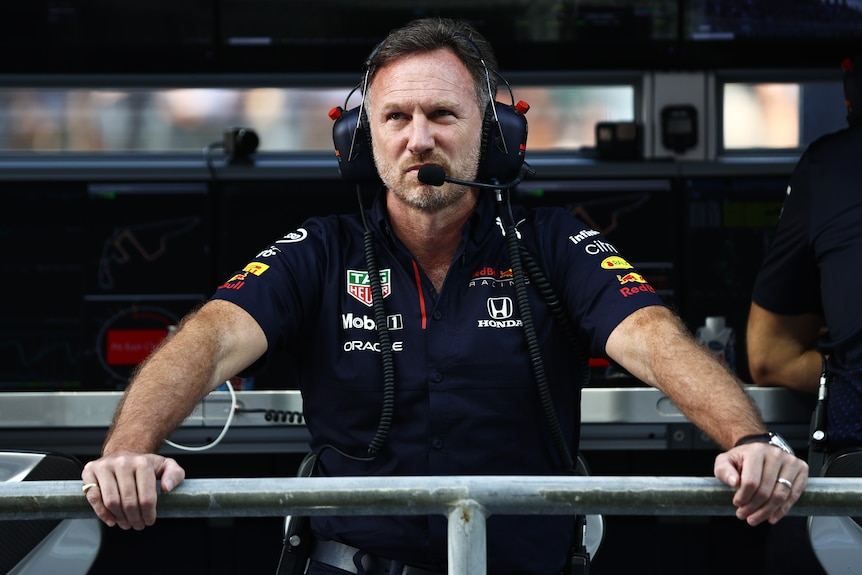 Motor racing team boss wearing a head set looks over the pit wall at a race.