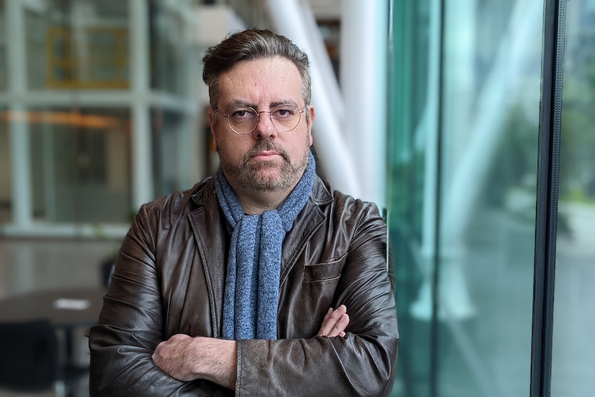 A man in a scarf and spectacles with his arms folded