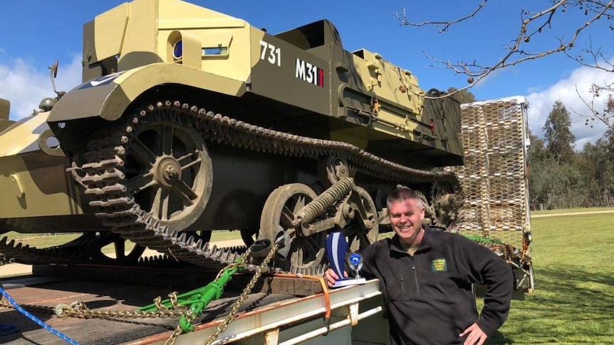 A man standing next to a tank-like machine on a flatbed truck.