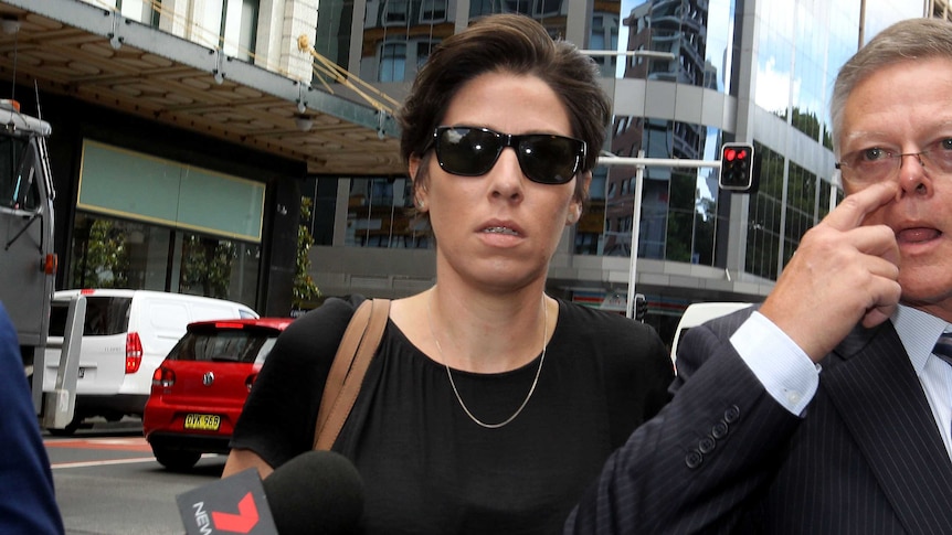 A close-up of a woman wearing sunglasses and walking outside a Sydney courthouse.