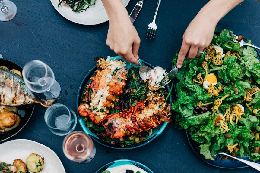 A crayfish is served on a plate next to salads and wine glasses