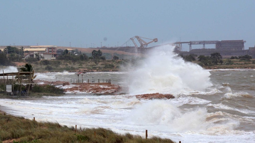 Waves being whipped up in heavy winds at a beach with port operations in the background.