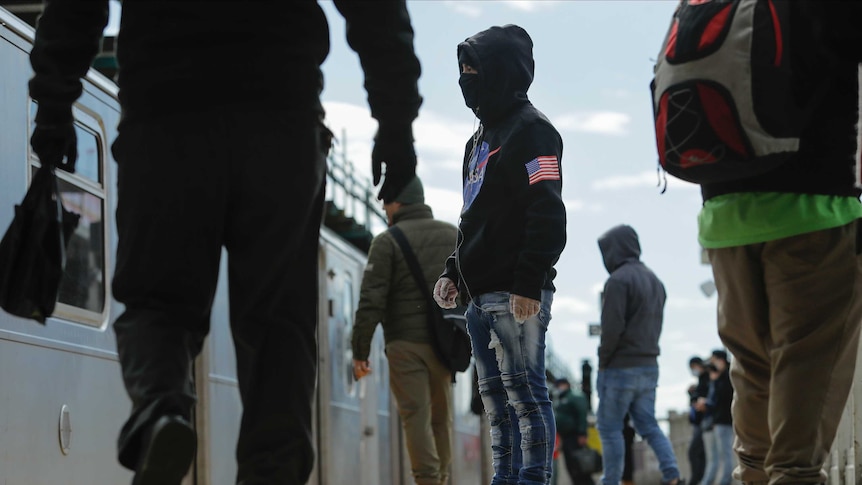 Pedestrians, including one with a face mask and a NASA hoodie board a train in the Queens borough of New York.