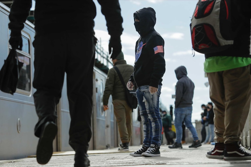 Pedestrians, including one with a face mask and a NASA hoodie board a train in the Queens borough of New York.