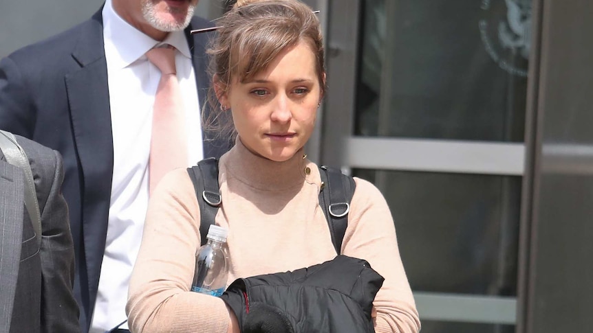 Allison Mack looks straight ahead while walking outside a court. She is carrying a jacket and wearing a backpack.