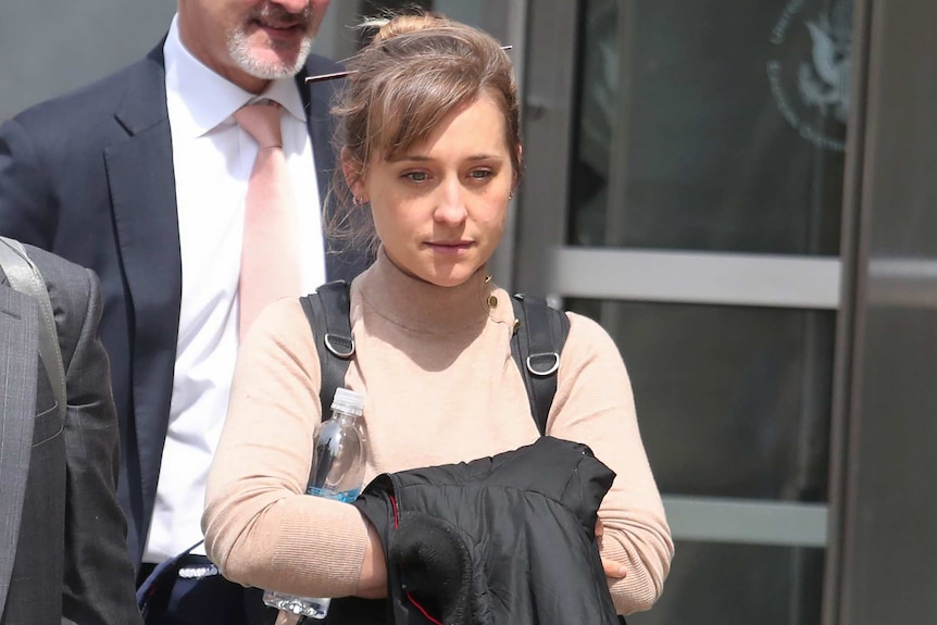 Allison Mack looks straight ahead while walking outside a court. She is carrying a jacket and wearing a backpack.