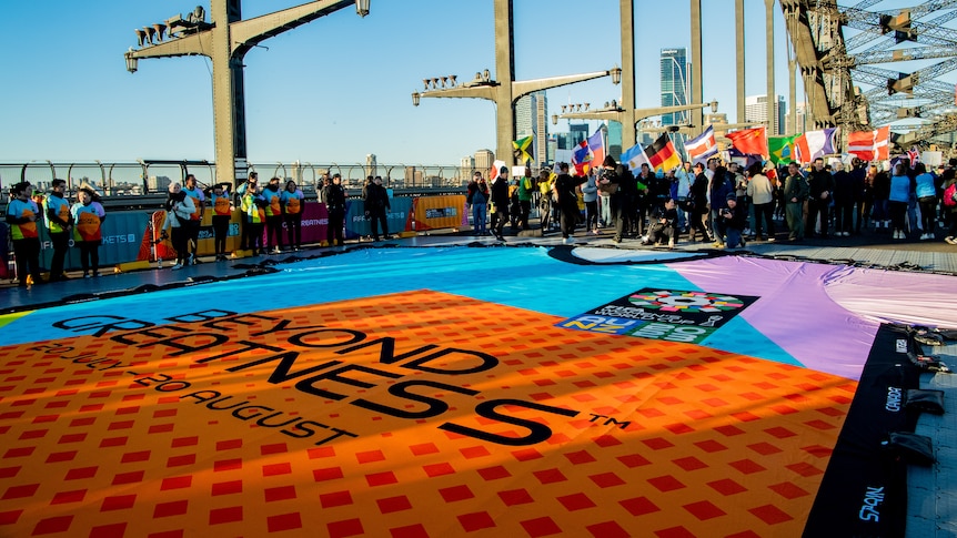 A giant multicoloured football jersey lies on the Sydney Harbour Bridge, with fans from multiple countries in the background.