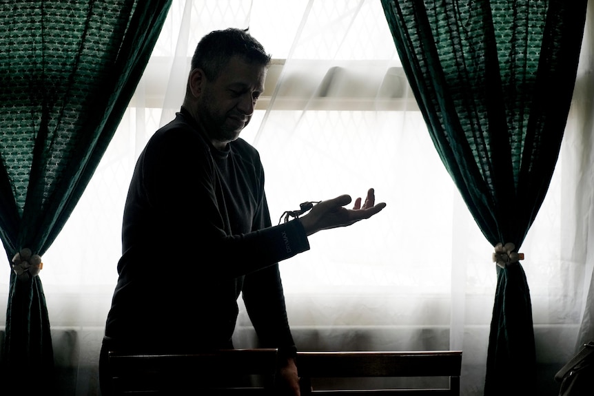 A man backlit by a bright window balances a large spider on his hand.