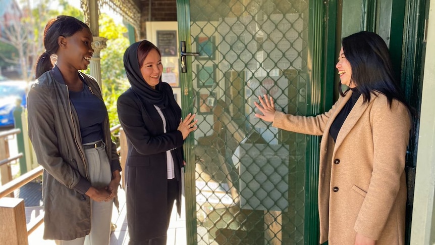 Three women stand at an open door smiling.