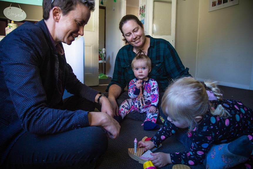 two women sitting on the floor, playing with their toddler and baby