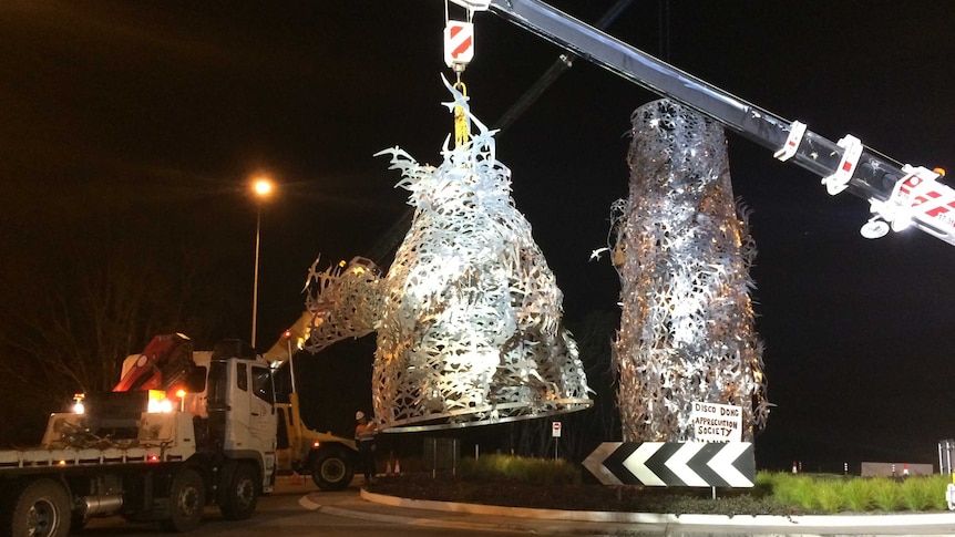 A crane lifts a metallic sculpture off a roundabout