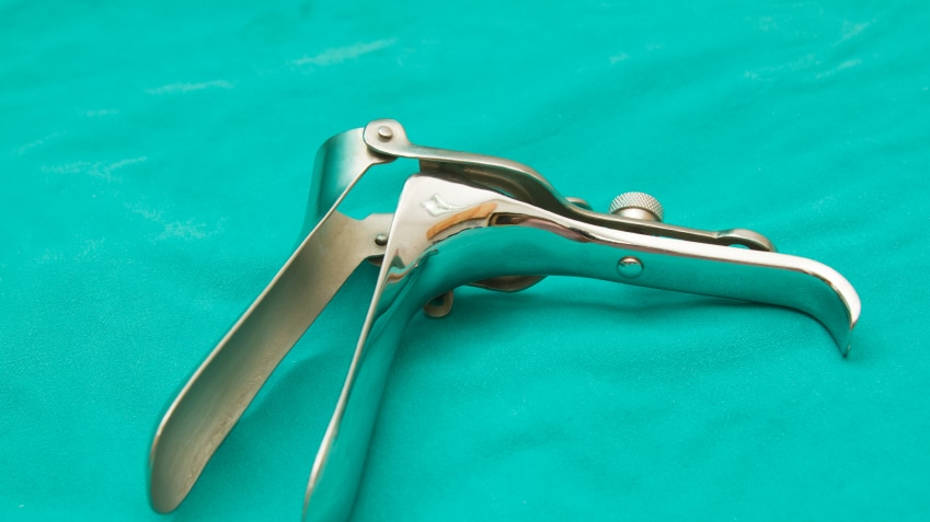 A metal gynaecological speculum, which is used in Pap smears, sitting on a green cloth.