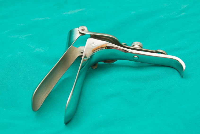 A metal gynaecological speculum, which is used in Pap smears, sitting on a green cloth.