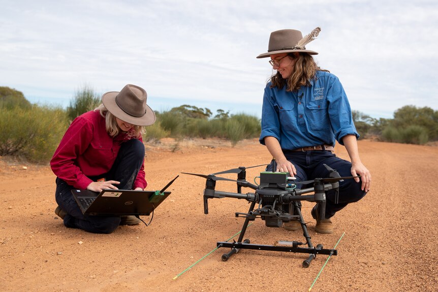 Two women crouching over a drone