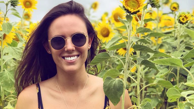 Young woman standing in a sunflower dress is a field of sunflowers.