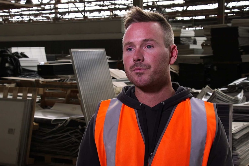 Clive Fleming stands in a fluoro vest in the middle of a solar panel recycling facility.