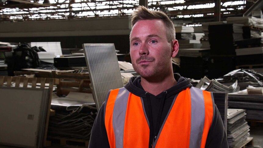 Clive Fleming stands in a fluoro vest in the middle of a solar panel recycling facility.
