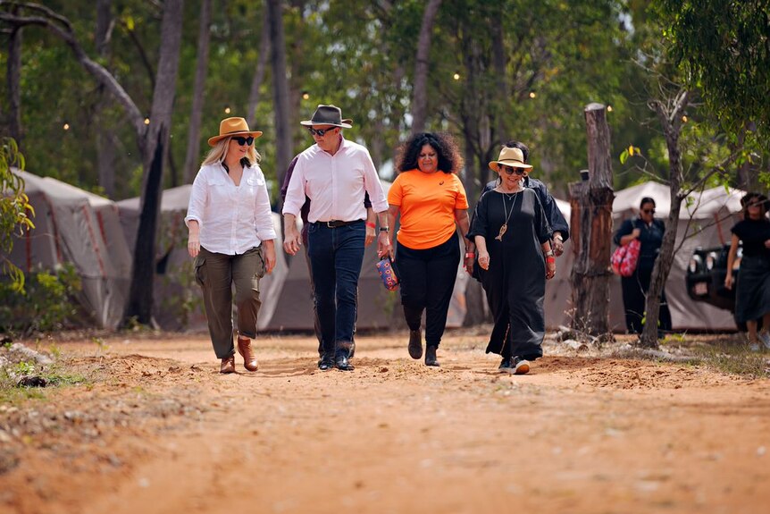 A man and three women walk along a dirt track in outback Australia.