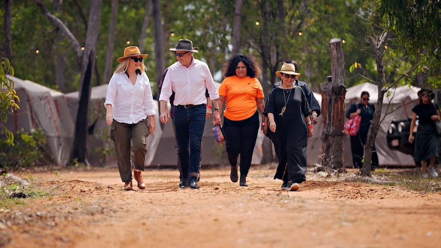 A man and three women walk along a dirt track in outback Australia.